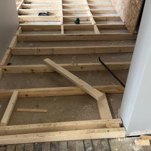Wooden floor frame under construction in a hallway with tools scattered.