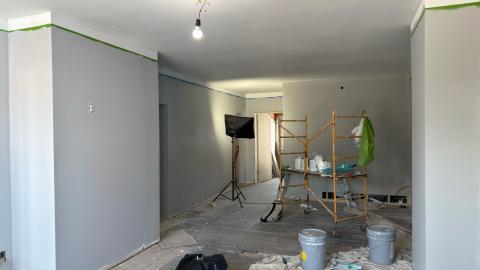 Room under renovation with grey walls, scaffolding, and painting supplies.