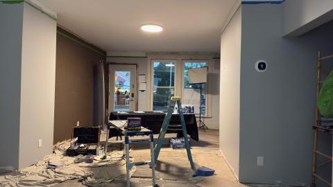 Renovation scene with ladder, tools, and paint supplies in a dimly lit room.