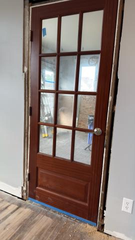 Wooden door with glass panels, partially installed in a room with gray walls.