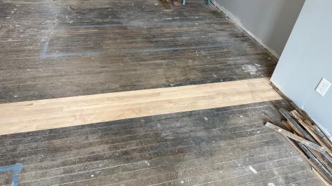 Old wooden floor with a strip of new wood in progress.