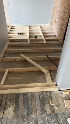 Wooden floor frame under construction in a hallway with tools scattered.